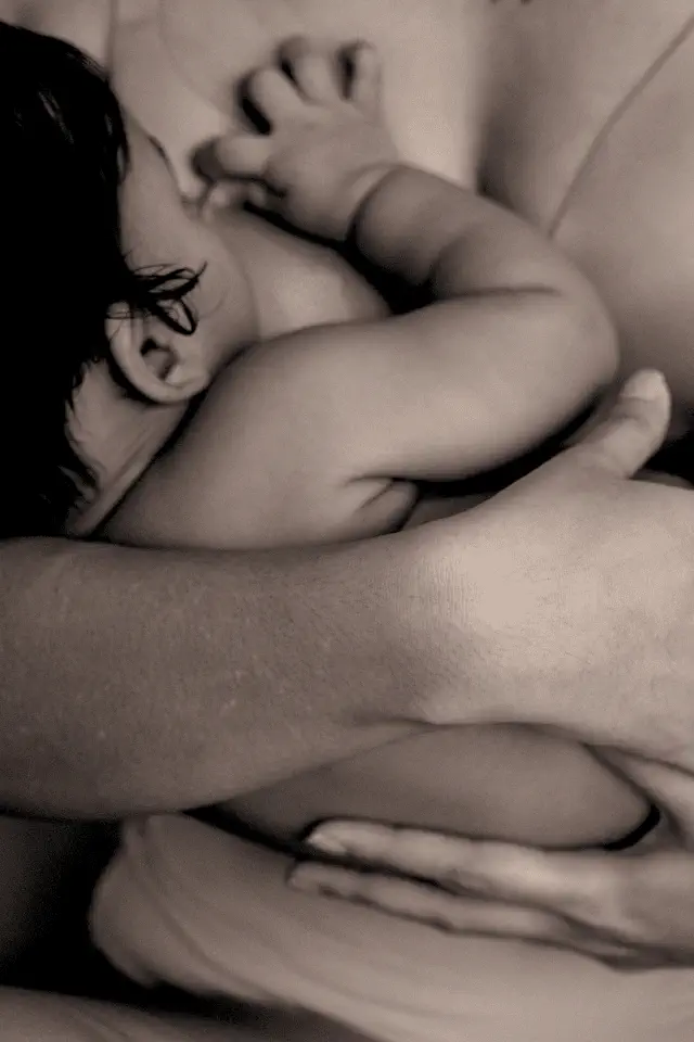 Neonato che succhia al seno della madre, simbolo del legame materno e dello sviluppo nei primi momenti di vita.