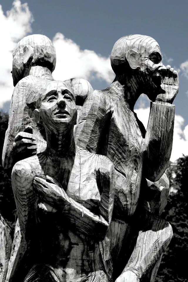 Scultura in legno che rappresenta figure umane espressive, simbolo dell'incomunicabilità e dell'isolamento emotivo.
