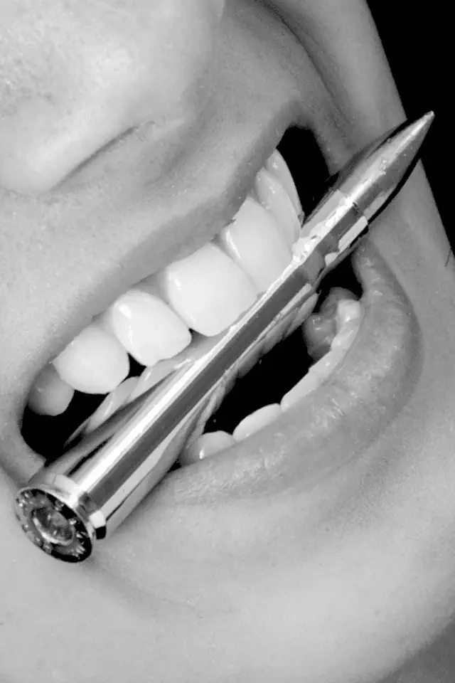 Bocca che stringe un proiettile tra i denti, metafora visiva del linguaggio armato e della necessità di smilitarizzare la parola.