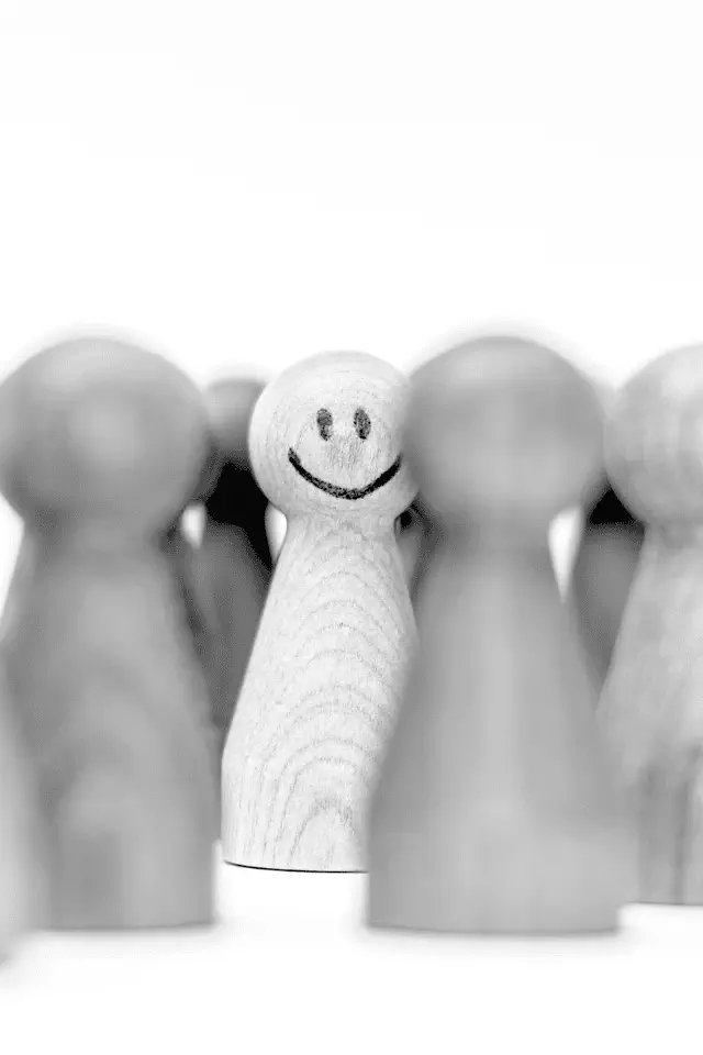 Birillo in legno con volto sorridente tra altri birilli sfocati: simbolo del potere di accontentarsi, trovando serenità in sé stessi.