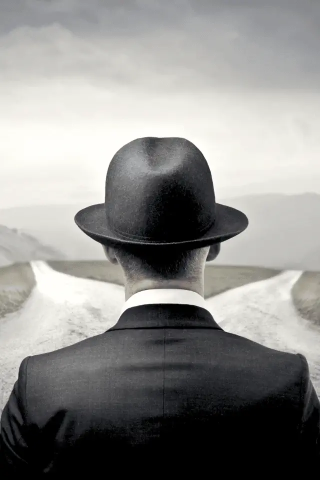 Uomo di spalle con cappello davanti a un bivio, simbolo della difficoltà di saper scegliere.
