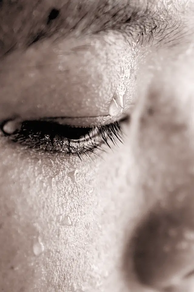 Dettaglio di un volto umano con gocce di sudore e lacrime che scorrono sulla guancia, simbolo della tristezza legata alla depressione estiva.