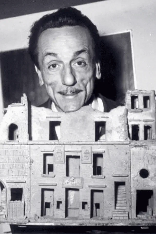 Eduardo De Filippo sorride dietro una scenografia teatrale in miniatura, simbolo della profondità dei pensieri interiori.