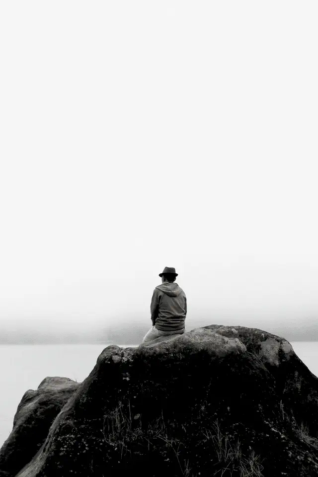 Persona seduta su una roccia davanti al lago, simbolo della solitudine e della riflessione.